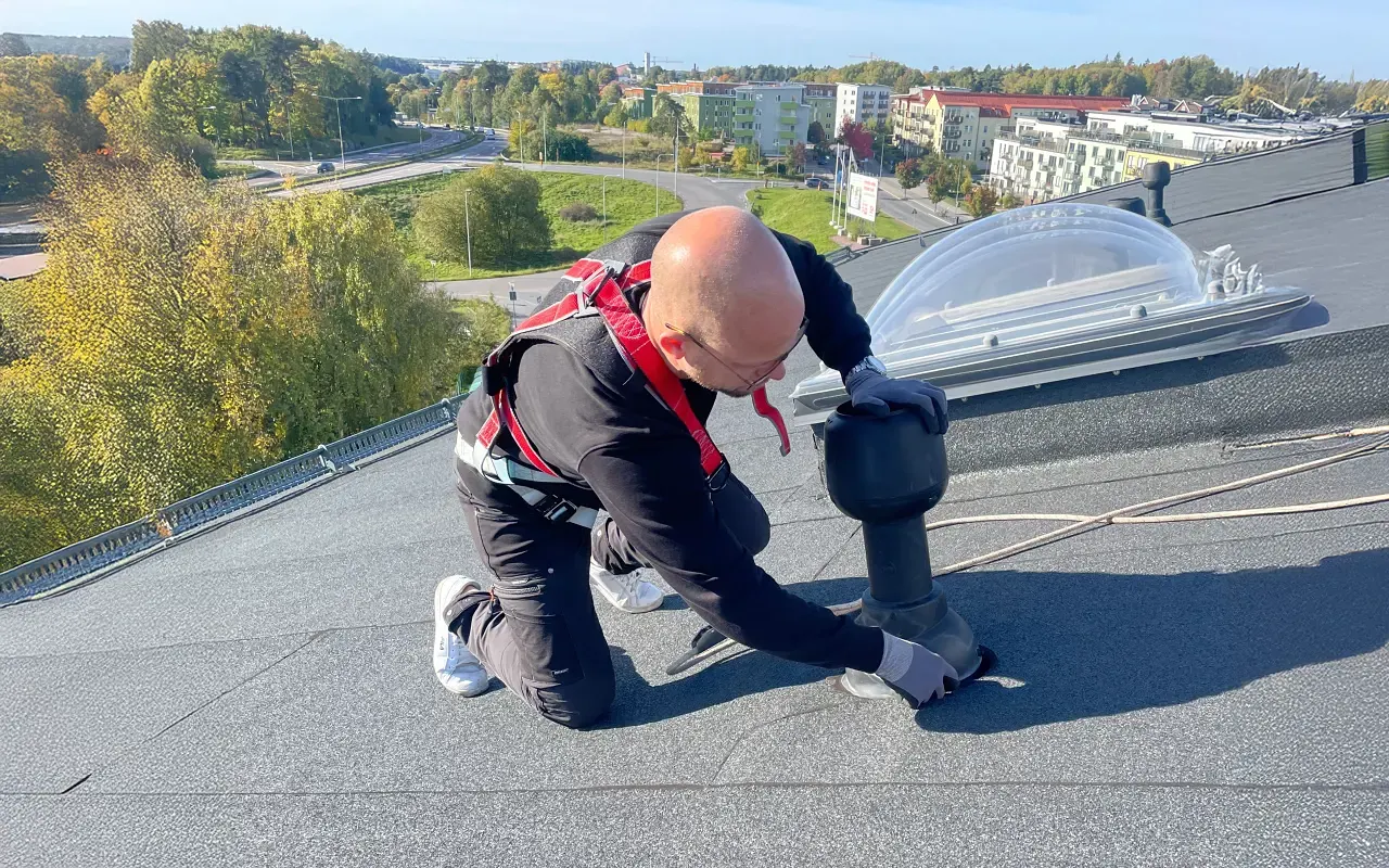 En takmontör med säkerhetssele arbetar på ett flackt tak.